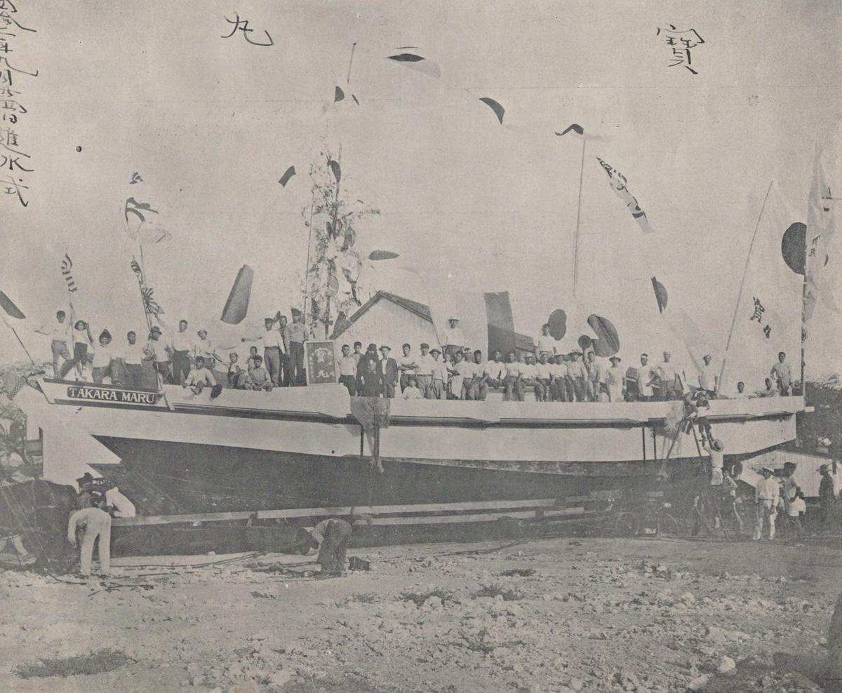A crowd of Japanese men, women and children gathered around a newly built fishing boat on the shore at Honolulu, around 1911