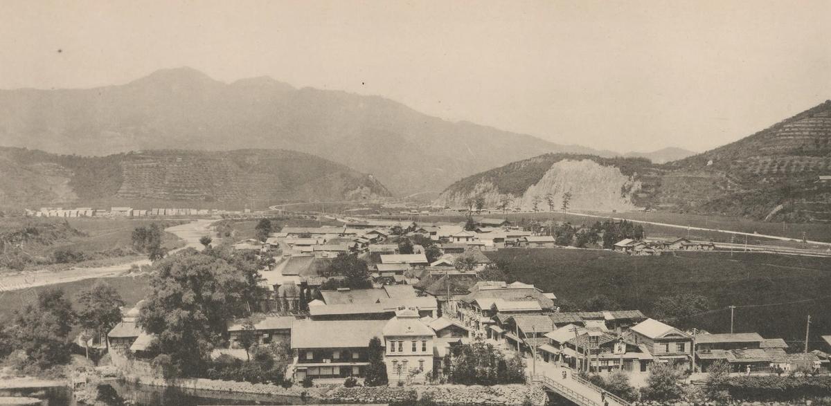 A hot-spring village of wooden houses along a river valley between wooded hills, Aomori Prefecture, 1915
