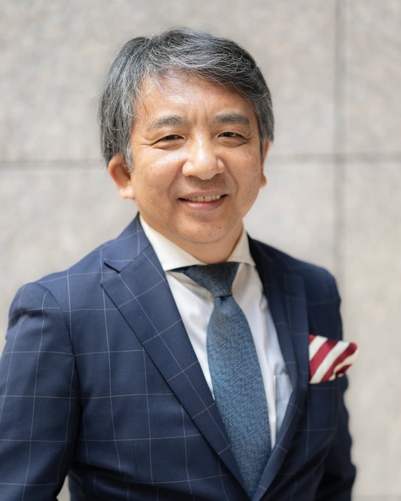 Mitsuru Otaka, smiling, in a navy check jacket and blue tie