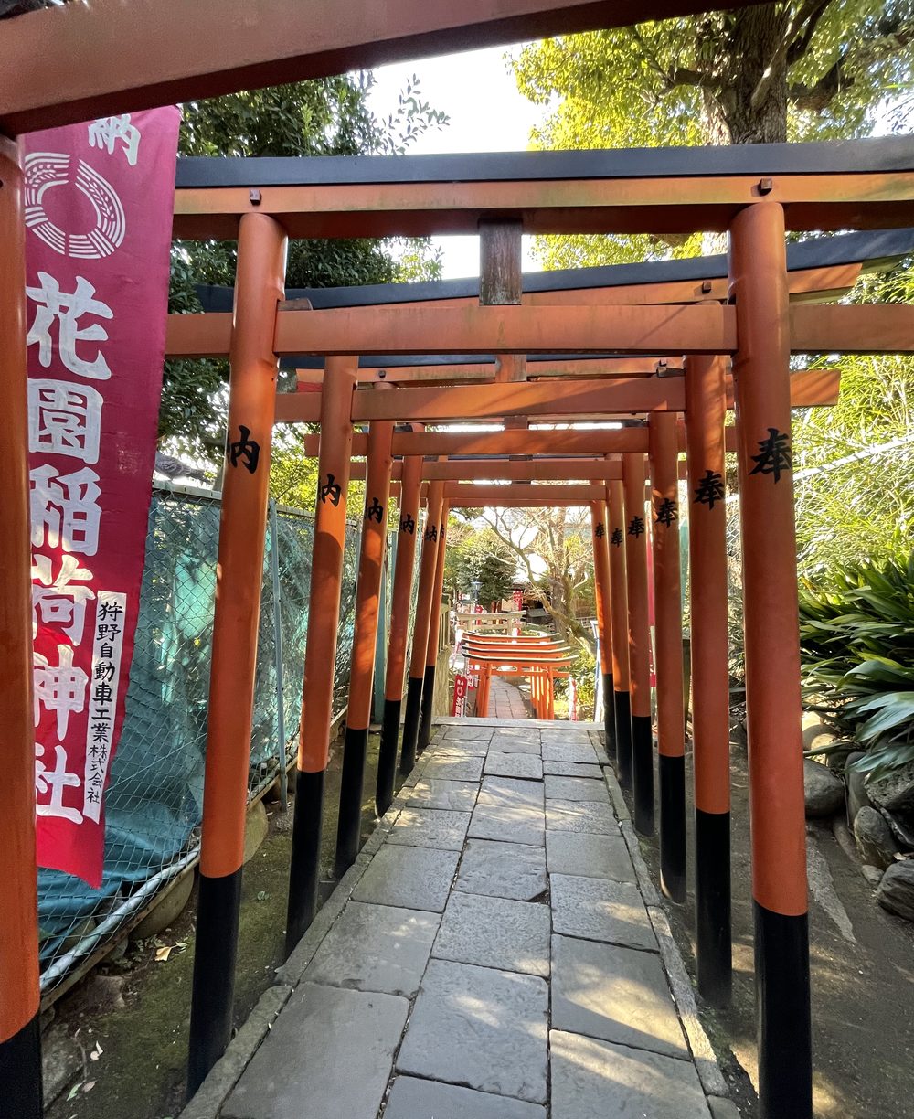 A stone path through a tunnel of red torii gates, with a red banner on the left